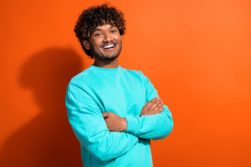 Portrait of handsome indian man curly hair crossed hands posing for local arabian outlet store isolated on orange color background
