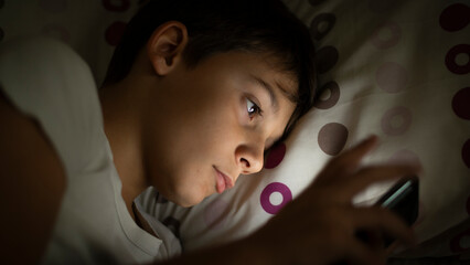 Child inside social networks with his smartphone from bed at night before sleeping. Concept of kids using social networks and their dangers without parental control at night from their room - obrazy, fototapety, plakaty