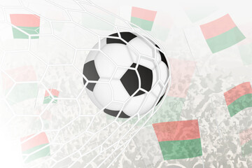 National Football team of Madagascar scored goal. Ball in goal net, while football supporters are waving the Madagascar flag in the background.