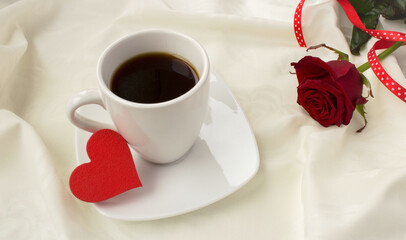 Coffee cup, red heart and red rose on the white textile background. Close-up.