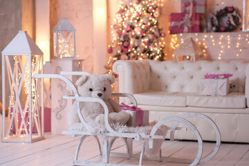 Christmas home interior- sled with white teddy bear, christmas tree, lights in white living room.