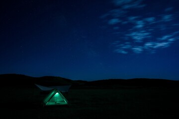 Cozy camping tent illuminated by the soft glow of the stars in a vast grassy landscape