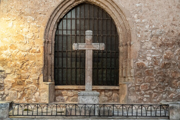 Medieval stone cross infront of the window of a church.