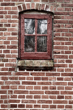 Old dirty window in a red brick house or home. Ancient casement with red wood frame on a historic building with clumpy paint texture. Exterior details of a windowsill in a traditional town or village