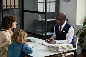 Portrait of senior black man consulting mother with child in insurance agency office - obrazy, fototapety, plakaty