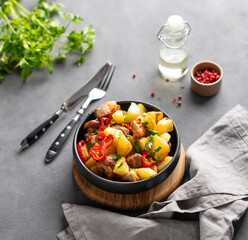 Fried pork meat with potatoes, onions and peppers. National homemade Georgian dish ojakhuri in a black frying pan on a dark background with spices and fresh herb.