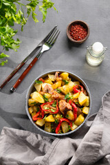 Fried pork meat with potatoes, onions and peppers. National homemade Georgian dish ojakhuri in a bowl on a dark background with shadow, spices and fresh herb.