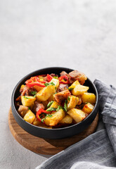 Fried pork meat with potatoes, onions and peppers. National homemade Georgian dish ojakhuri in a black bowl on a light background with shadows and napkin.