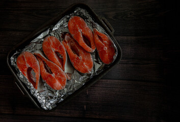 Raw fish trout steak on board on black background with lemon and spices