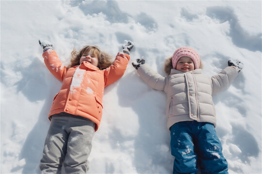 little kids playing in snow, making snow angels in winter