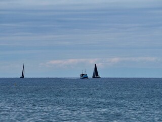 Sailboats float in the middle of a serene sea against a clear blue sky