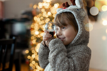 A little boy in a warm pajamas plays with a prism ball against the backdrop of Christmas lights....