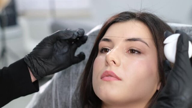 Specialist marks the clients eyebrows before procedure with special thread.