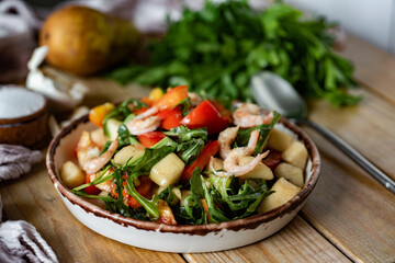 Breakfast for the whole family: salad with shrimp, arugula, fresh tomatoes and olive oil in a beautiful plate on wooden boards. Close-up