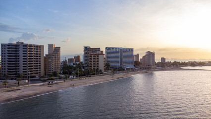 Drone photos of the City of Lechería on a sunset, in which you can see buildings, sea, people bathing on the beach, and passers-by.
Playa los Canales Boulevard