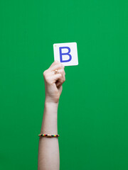 Lettre en carton et bois tenue par une main d'enfant sur fond vert détourage facile pour création...