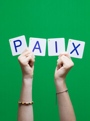 Mot PAIX en carton et bois tenue par une main d'enfant sur fond vert détourage facile pour...