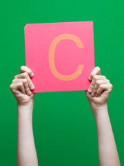 Lettre en carton et bois tenue par une main d'enfant sur fond vert détourage facile pour création...