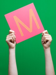 Lettre en carton et bois tenue par une main d'enfant sur fond vert détourage facile pour création...