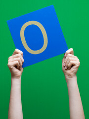 Lettre en carton et bois tenue par une main d'enfant sur fond vert détourage facile pour création...