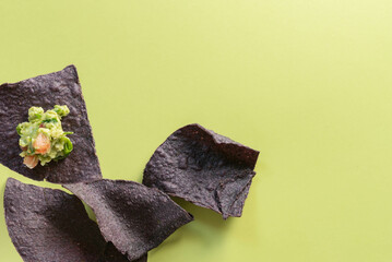 Organic blue corn tortilla chips with a bite of chunky, guacamole on a bright green background.