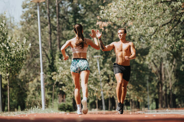 Fototapeta premium Fit sports couple sprint and jog in sunny park for outdoor training. Practicing together in sportswear, they motivate each other to achieve better body shape, strong muscles, and positive results.