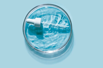 Liquid pipette serum blue gel on light cyan colored Petri dish background