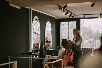 Beautiful hairdresser brushing her clients hair and talking to her while standing at the hair salon