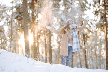 A young woman throws out snow. Portrait of a happy woman playing with snow on a sunny winter day. A walk through the winter forest. Concept of fun, relaxation.