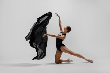Graceful young ballerina practicing dance moves with black veil on white background