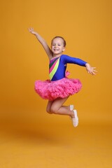 Cute little dancer in costume jumping on orange background