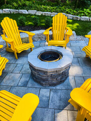 Yellow Muskoka chairs in a circle around a beautiful stone fire pit in estate residential backyard...
