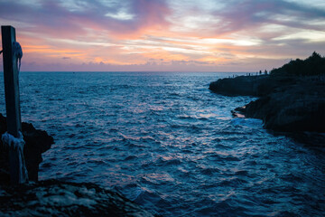 Sunset hues over a rugged coastline with silhouettes of onlookers