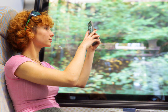 teenage girl takes picture landscape through window while sitting in train carriage