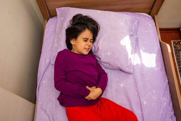 Top view of a little girl lying in bed with abdominal pain
