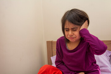 Primary school age girl sitting on her bed with earache