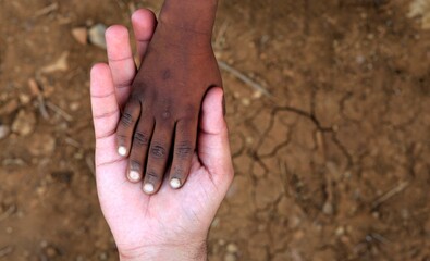 Close-up of an adult white hand holding the hand of a black child.