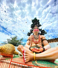 In this captivating picture, a grand statue of Lord Hanuman stands tall and resplendent, an...