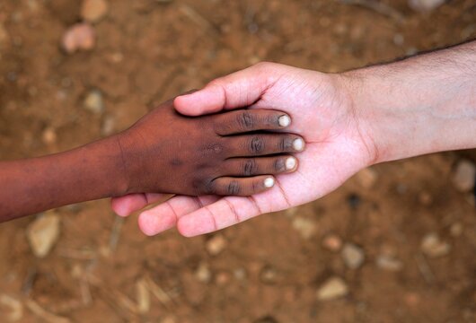 Close-up of an adult white hand holding the hand of a black child.