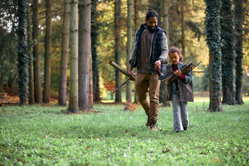 Black little girl and her father collecting tree branchers for campfire while spending day in forest