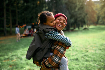 Cheerful black mother and daughter embracing while enjoying in camping day in  woods.