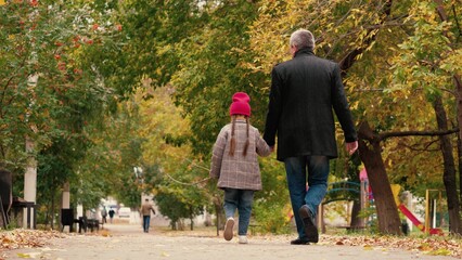 Fototapeta na wymiar Happy little girl talks to caring father walking along autumn park road