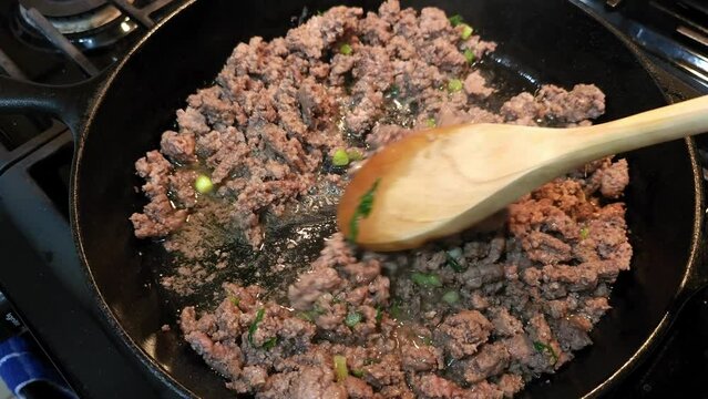 Ground beef cooking in cast iron pan with green onions