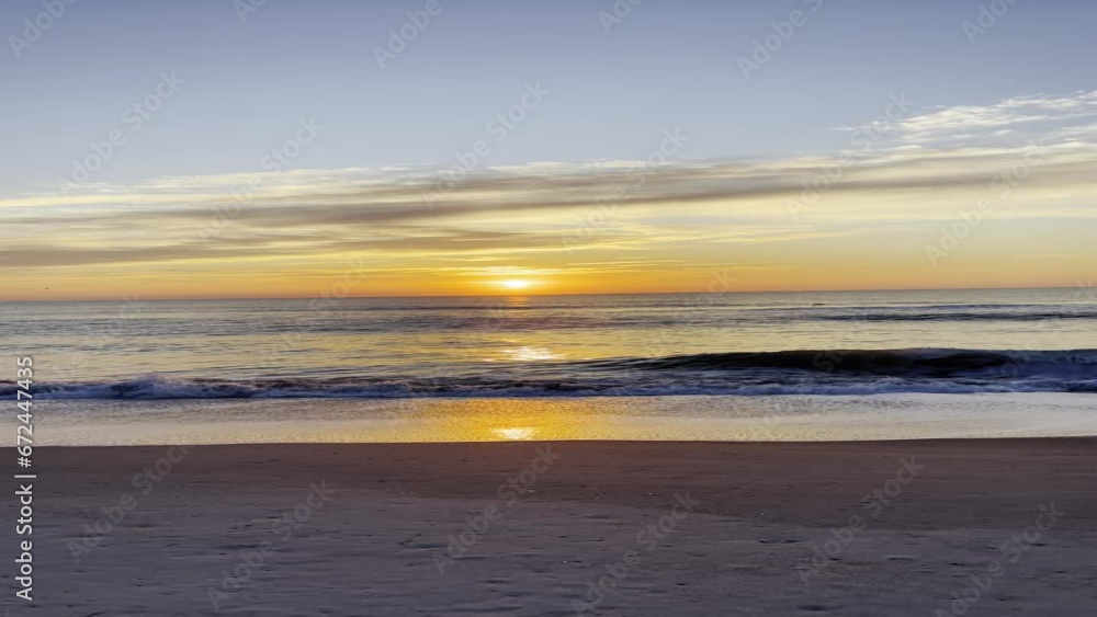 Sticker Vertical scene of dusk sunset sky reflecting on sea waves splashing on sandy beach