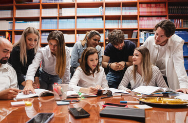 Young group of students discussing and working on a project with their professors in a library
