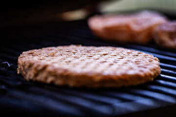 Raw, frozen beef patty placed on the grill grate