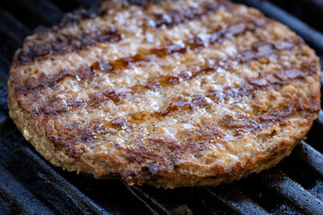 A close-up of a succulent beef burger patty positioned on the barbecue griddle already grilled on one of its sides