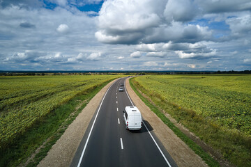 Aerial view of intercity road between green agricultural fields with fast driving cars. Top view from drone of highway traffic