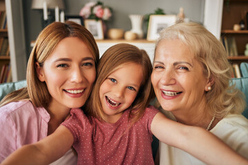 Happy grandmother, mother and granddaughter taking selfies at home