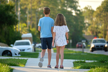 Rear view of two young teenage children, girl and boy, brother and sister walking together on rural street on bright sunny day. Vacation time concept